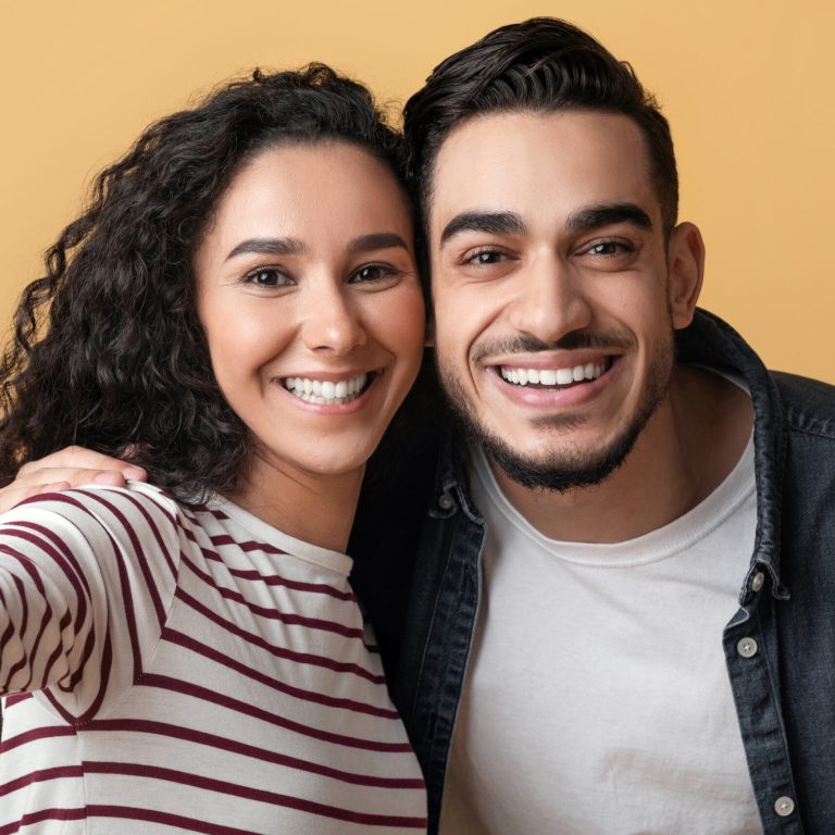 Cheerful Young Middle Eastern Couple Taking Selfie Together, Happy Millennial Arab Man And Woman Smiling At Camera, Joyful Spouses Posing Together Over Yellow Studio Background, Closeup POV Shot